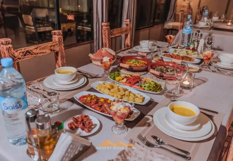 Table de dîner avec des plats marocains dans l’espace restaurant du Desert Rose Camp à Merzouga