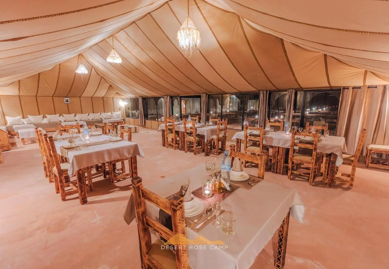 Intérieur du restaurant au Desert Rose Camp à Merzouga avec des chaises en bois rustiques et des tables dressées