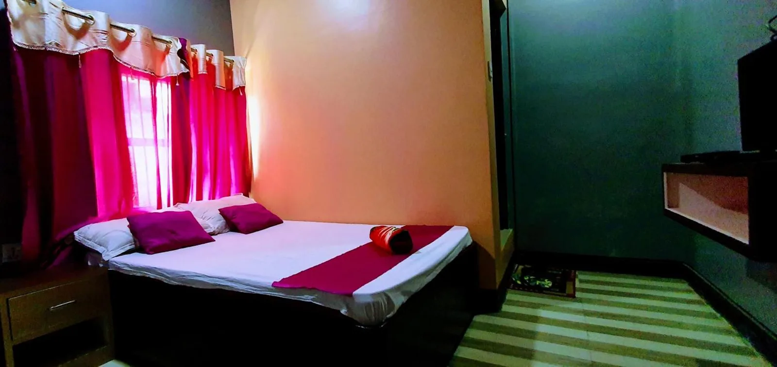 Una habitación de huéspedes compacta en Devtara Himalayan Hotel en Lumbini con cama, cortinas y estante para televisión