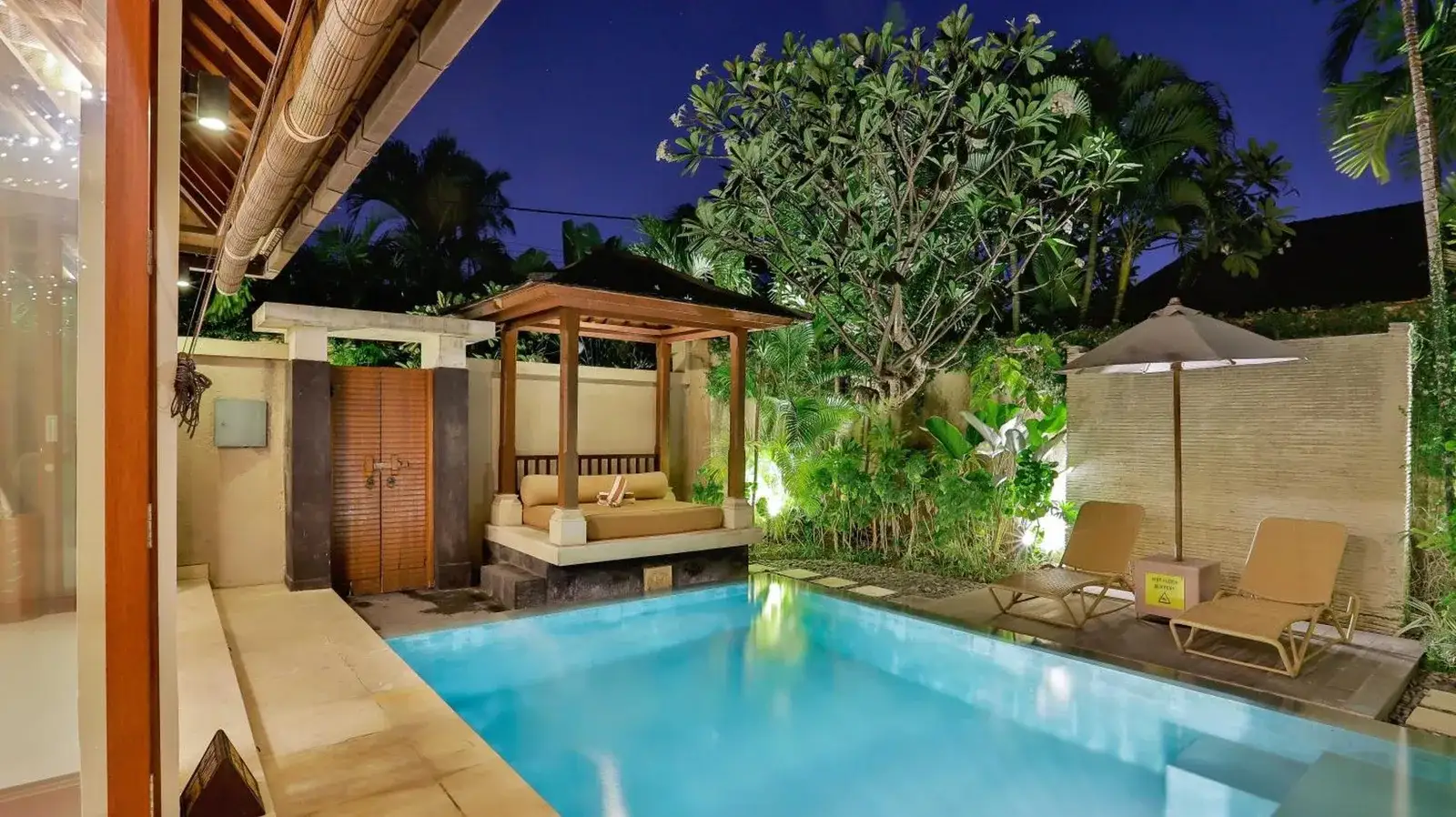 Nighttime private pool terrace at DISINI Luxury Spa Villas-CHSE Certified in Seminyak with daybed, loungers, and tropical landscaping
