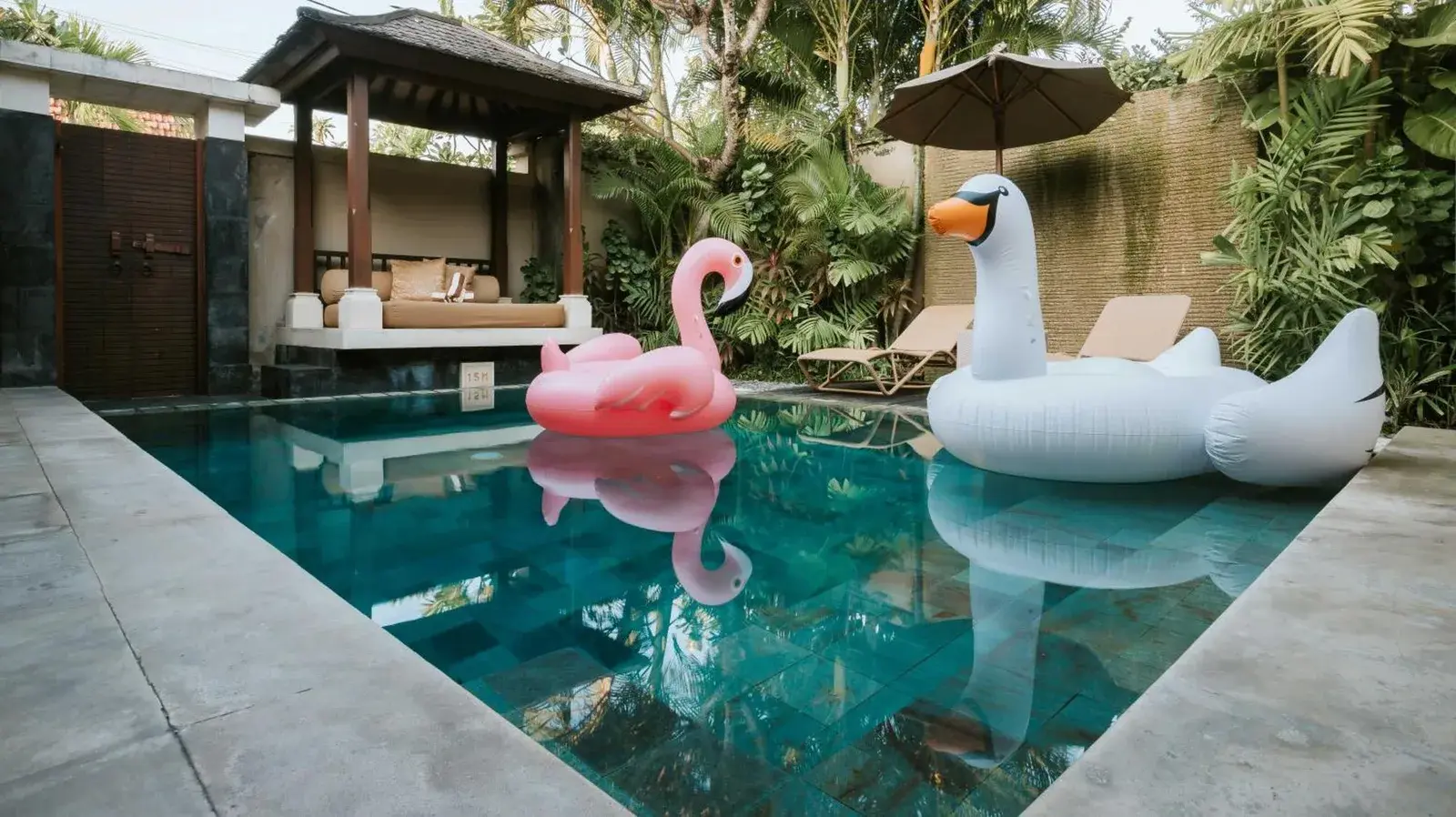 Private pool at DISINI Luxury Spa Villas-CHSE Certified in Seminyak with flamingo and swan floats in a tropical courtyard
