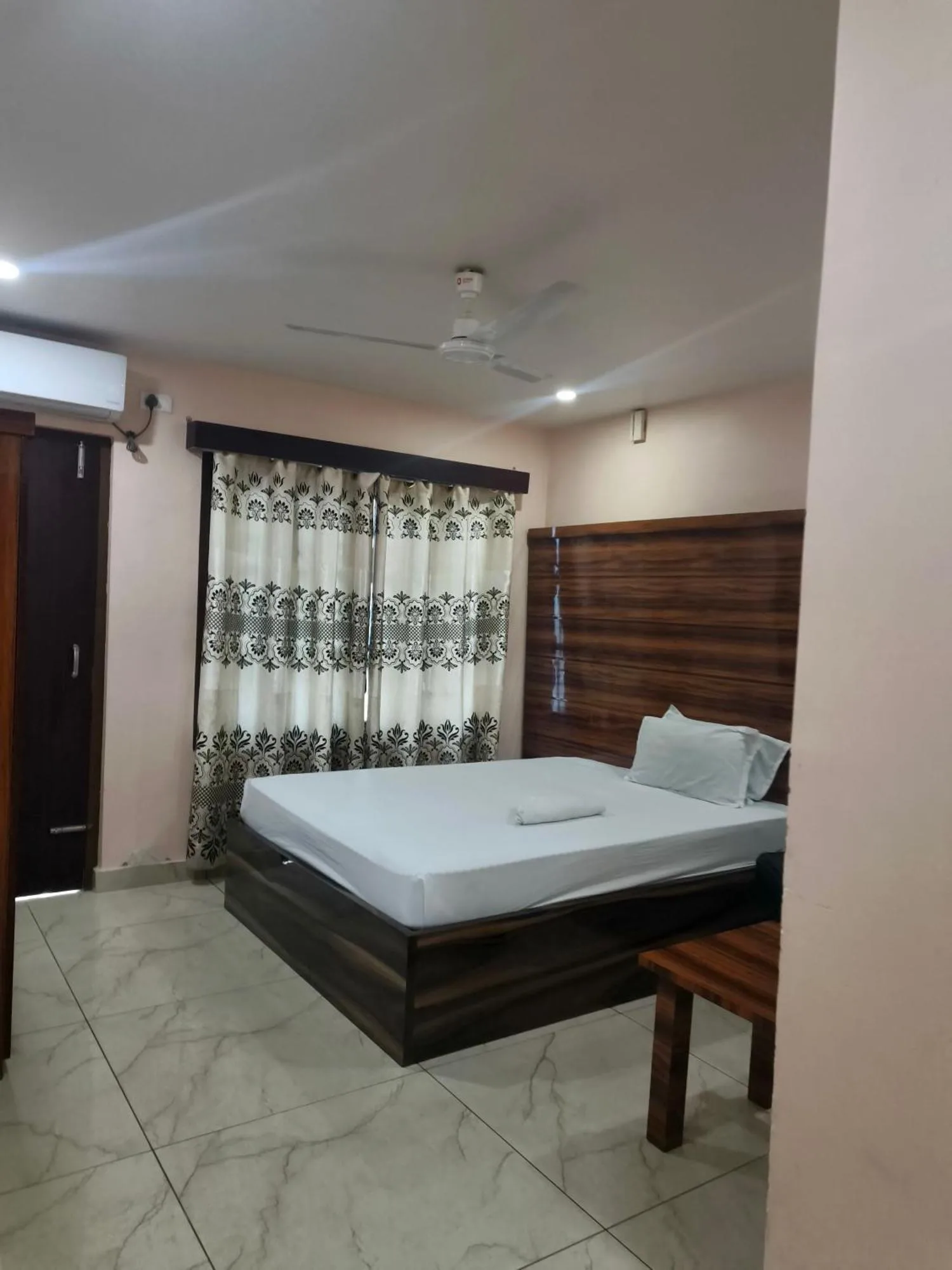 Dormitorio de Domukha Pali Ghar en Birtamod con TV montada en la pared, cama y mesa de estar.