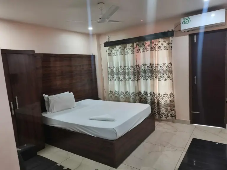 Dormitorio elegante de Domukha Pali Ghar en Birtamod con una cama grande, muebles de madera y aire acondicionado.