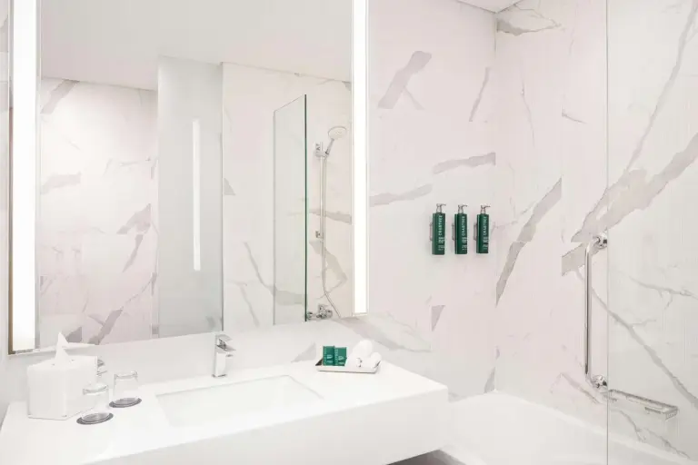 Baño moderno en DoubleTree by Hilton Fujairah City con paredes de estilo mármol, lavabo de tocador y bañera.
