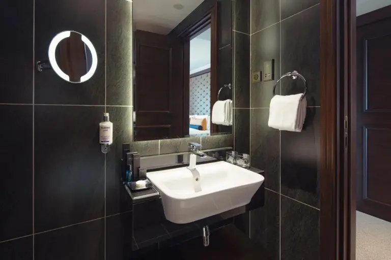Lavabo et miroir de salle de bains au Dukes The Palm Dubai Hotel à Dubai avec murs carrelés sombres.