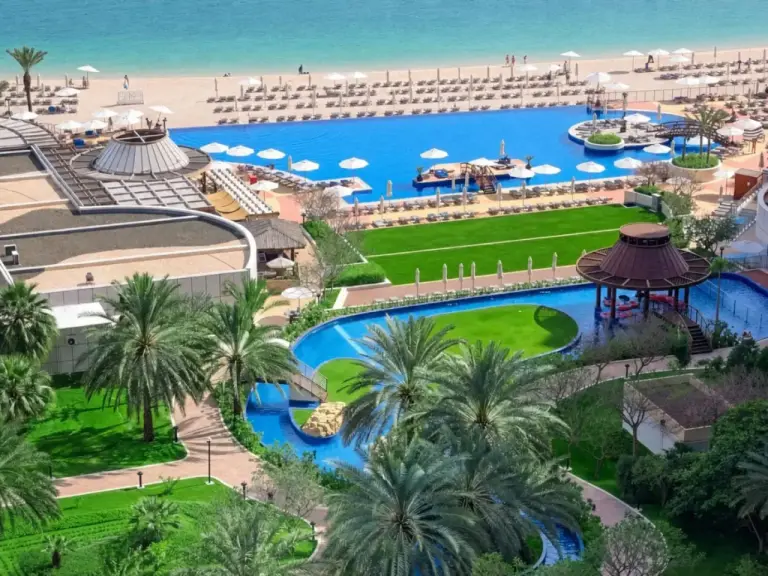 Vue extérieure de Dukes The Palm Dubai Hotel à Dubai avec piscines, transats de plage et jardins paysagers.