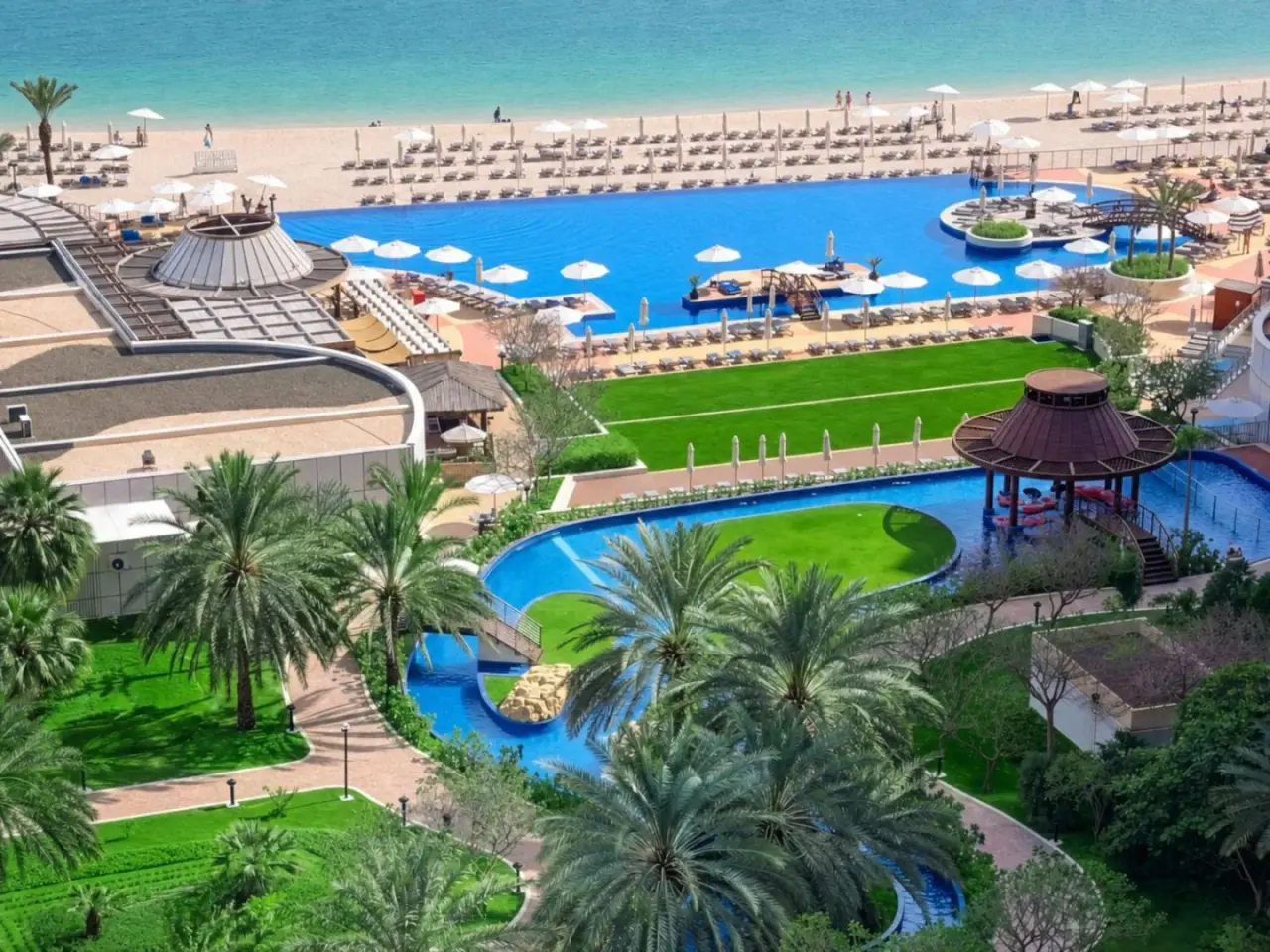 Vue extérieure de Dukes The Palm Dubai Hotel à Dubai avec piscines, transats de plage et jardins paysagers.
