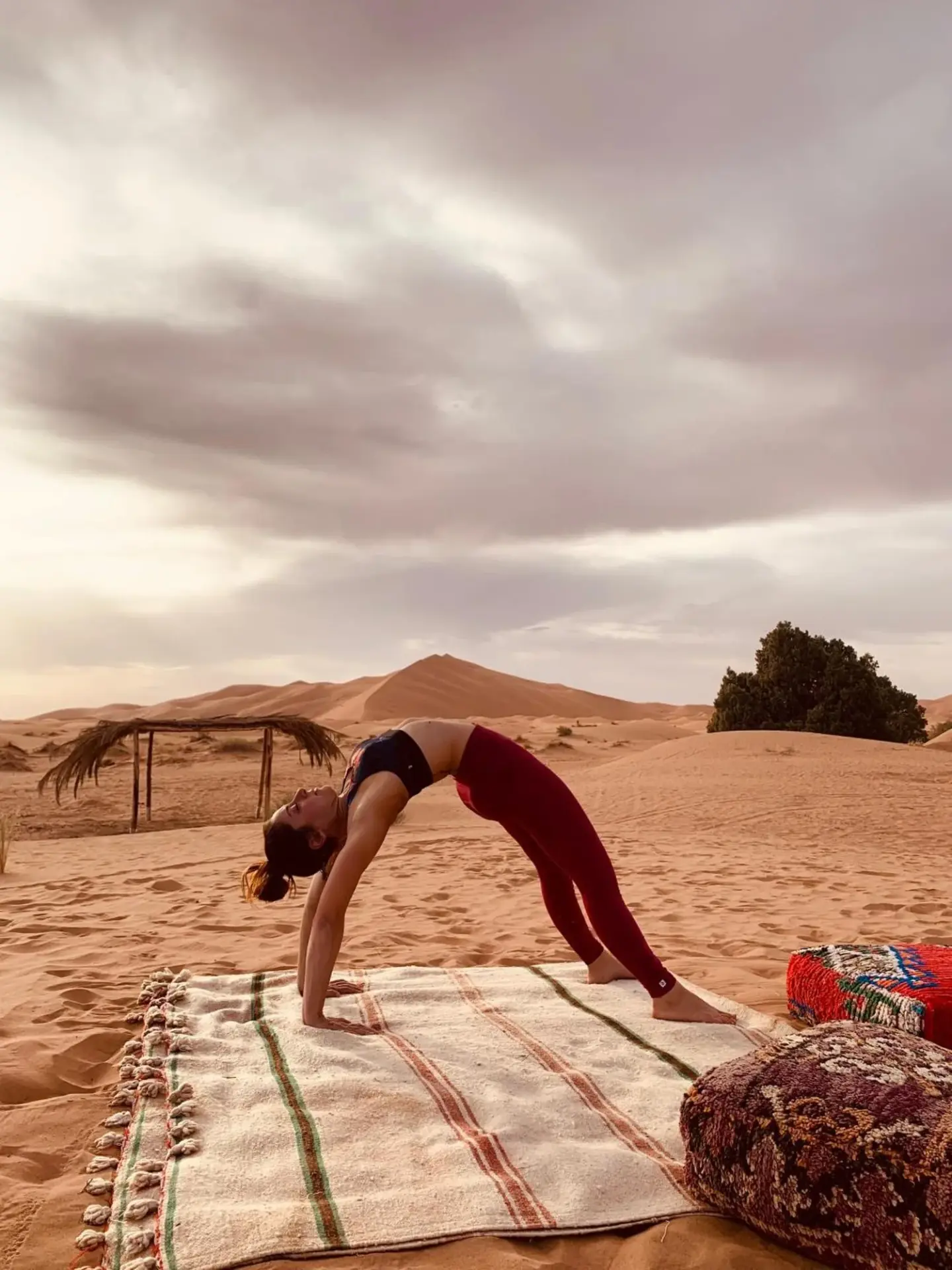 Eco Merzouga luxury camp in Merzouga with a guest doing yoga on a rug in the desert