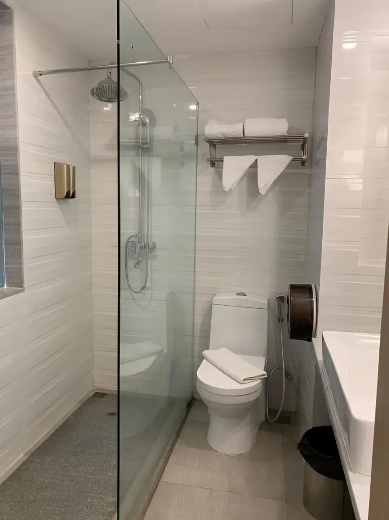 Modern bathroom at Elong Hotel Pattaya Jomtien Beach with glass shower, toilet, and white tile walls