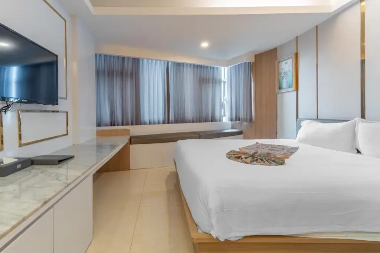 Spacious guest room at Elong Hotel Pattaya Jomtien Beach with king bed, curtains, and bedside table