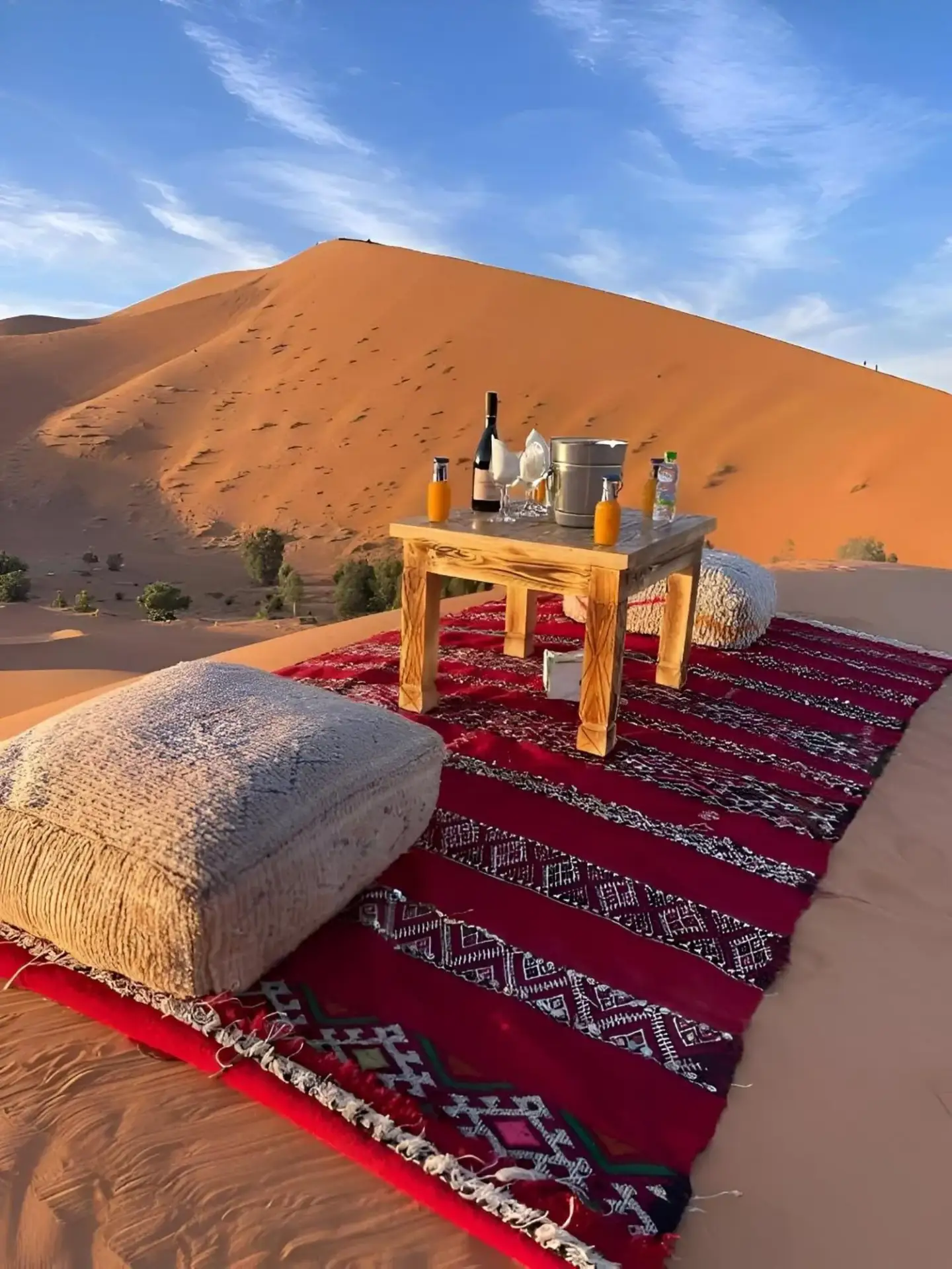Installation de repas dans le désert à Endless Sahara Camp à Merzouga avec une table sur un tapis surplombant les dunes de sable.