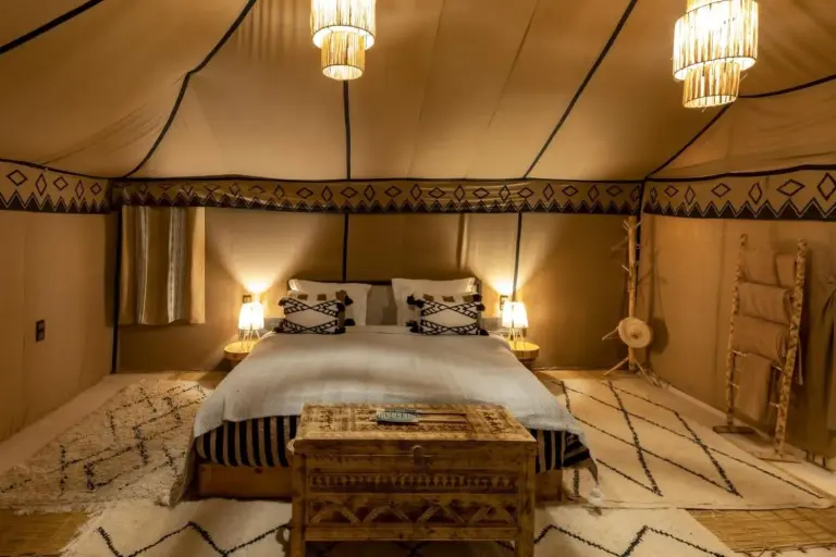Bedroom inside Erg Chebbi Desert Camp And Activities in Merzouga with a double bed, rugs, and woven lamps.