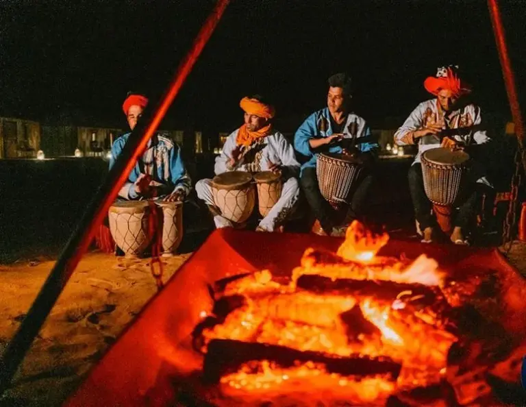 Traditional drumming performance at Erg Chebbi Desert Camp And Activities in Merzouga beside a campfire at night.