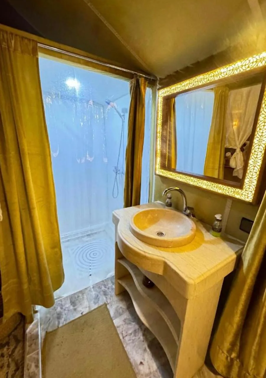 Baño de Expedition Luxury Camp en Merzouga con lavabo, espejo y zona de ducha dentro de una tienda de lujo