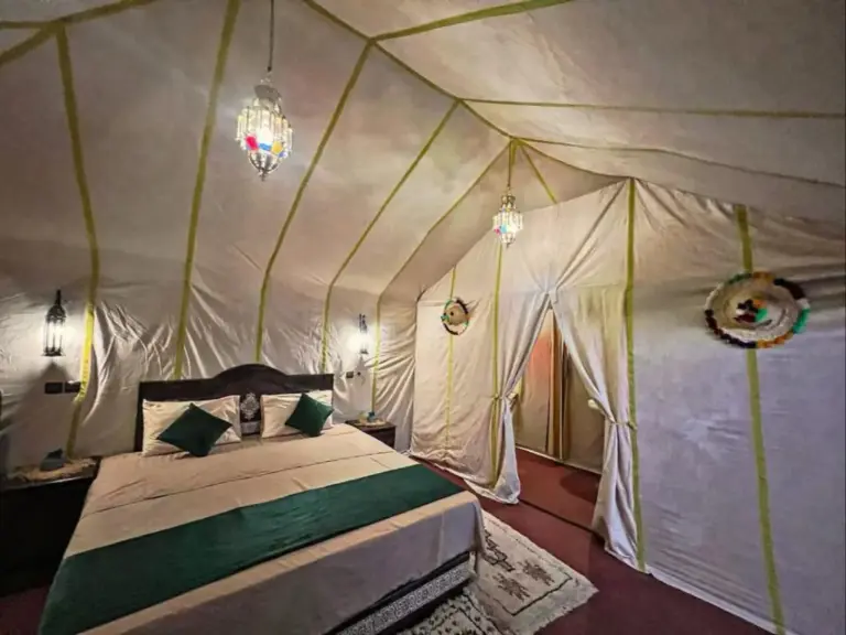 Tienda dormitorio de Expedition Luxury Camp en Merzouga con cama doble, detalles en verde y faroles colgantes