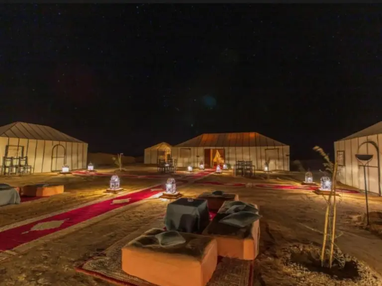 Exterior nocturno de Expedition Luxury Camp en Merzouga con tiendas del desierto iluminadas y asientos de salón