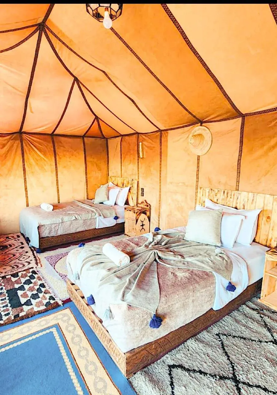 Habitación con tienda doble de Expedition Luxury Camp en Merzouga con dos camas, iluminación cálida y alfombras estampadas