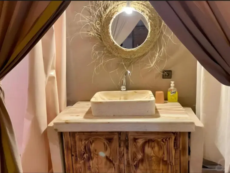 Zona de tocador de Expedition Luxury Camp en Merzouga con mueble de lavabo de madera y decoración de espejo trenzado