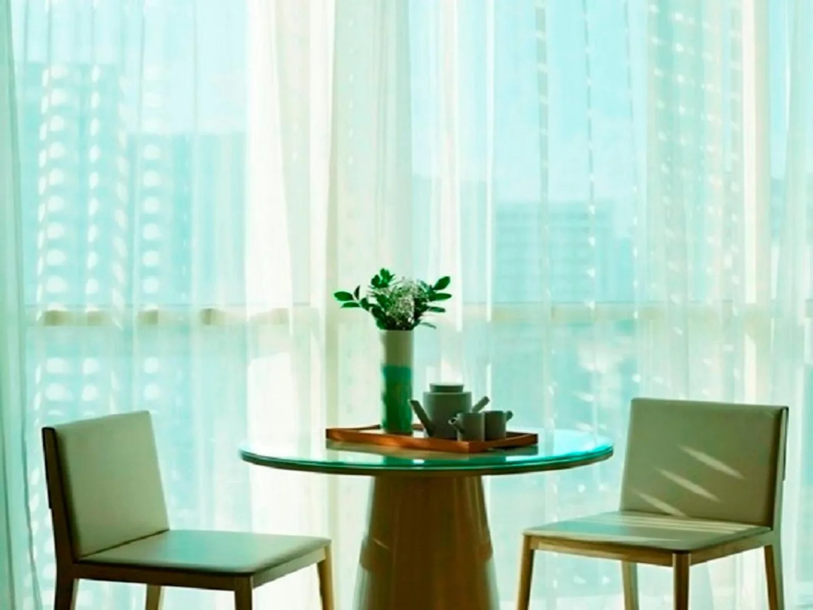 Rincón de comedor en Fraser Residence Menteng Jakarta con mesa redonda de cristal y sillas junto a la ventana