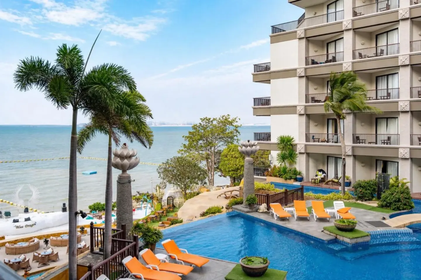 Zone de piscine extérieure au Garden Cliff Resort And Spa à Pattaya avec vue sur l’océan, palmiers et chaises longues