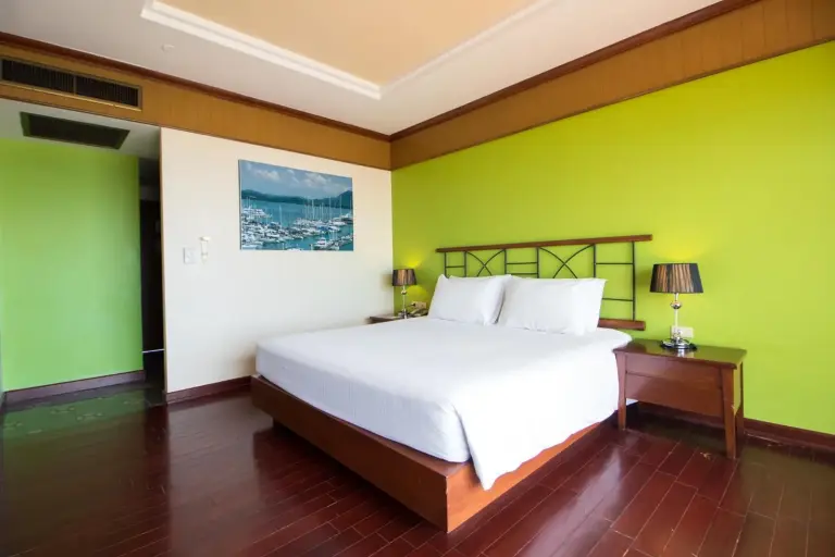 Chambre avec lit king-size à Garden Sea View Resort Pattaya avec mur vert vif et mobilier en bois.