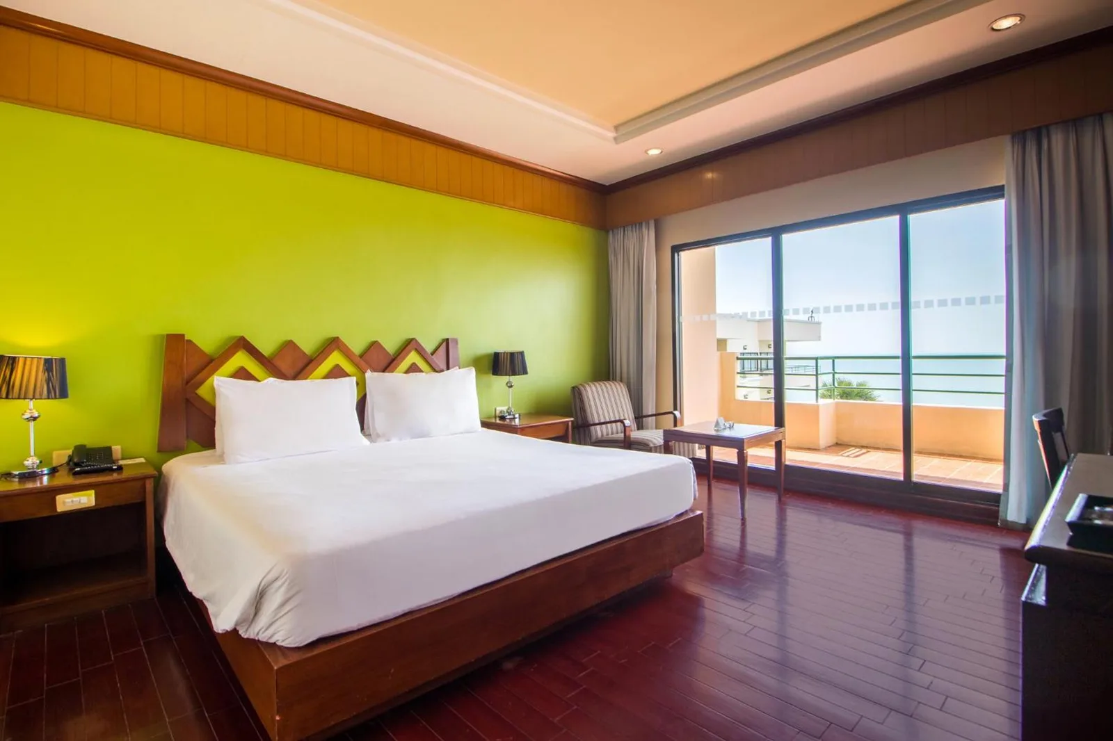 Chambre avec lit king-size à Garden Sea View Resort Pattaya avec balcon et vue sur l’océan.