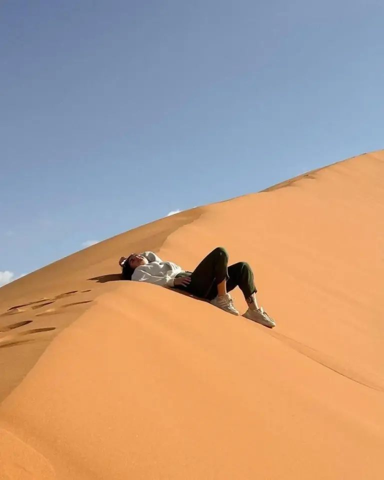 Client se détendant sur une dune de sable près de Glamping Under Stars à Merzouga, profitant du paisible paysage désertique.