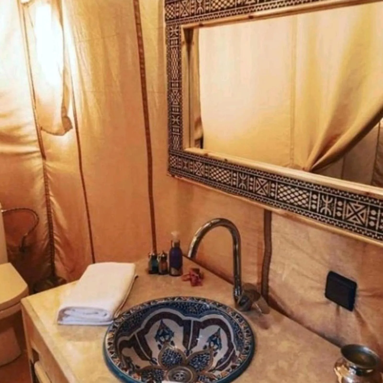 Salle de bains élégante sous tente à Glamping Under Stars à Merzouga avec un lavabo à motif, un miroir et un espace lavabo compact.