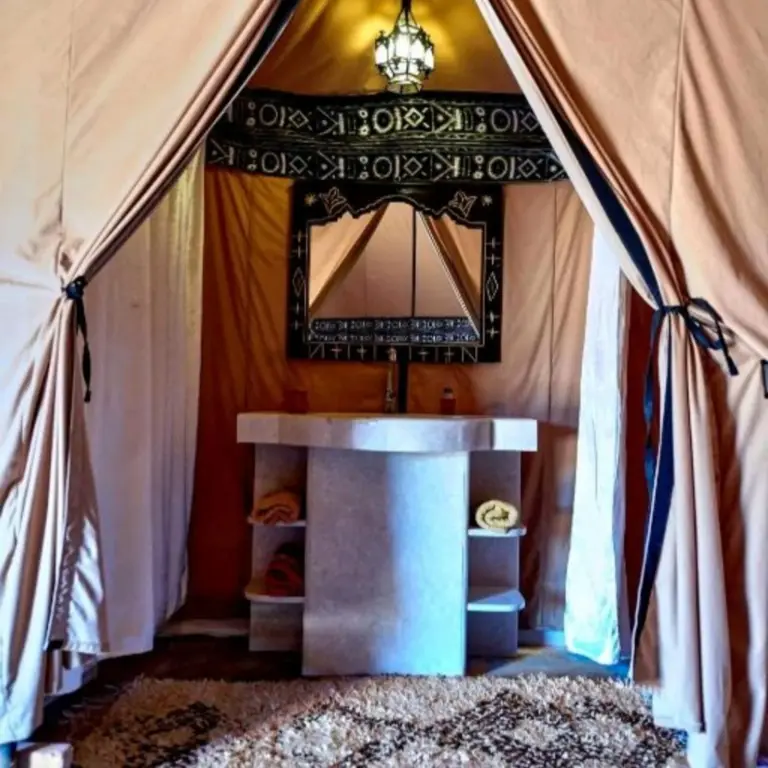 Salle de bains traditionnelle sous tente à Glamping Under Stars à Merzouga, avec un lavabo, un miroir et une décoration chaleureuse de style désertique.
