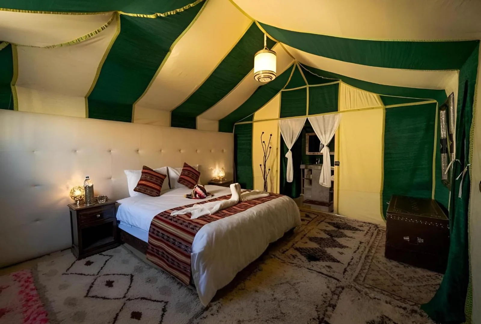 Luxury tent room at Golden Dunes Luxury Camp in Merzouga with a double bed, patterned textiles, and green-and-cream canvas walls.