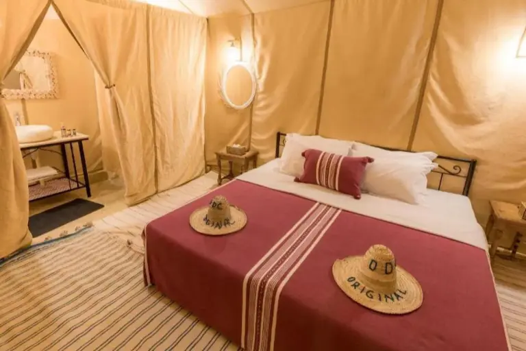 Private tent bedroom at Golden Dunes Luxury Camp in Merzouga with a double bed, maroon bedding, and ensuite area.