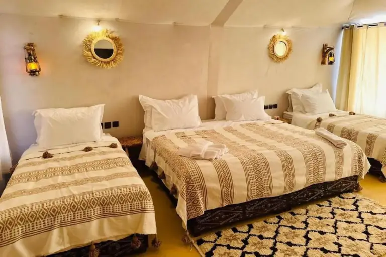 Triple room at Golden Dunes Luxury Camp in Merzouga with three beds, soft lighting, and beige patterned bedding.