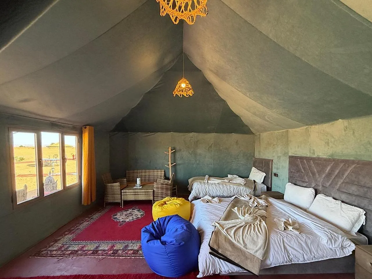 Deluxe tent room at Gorgeous Luxury Camp in Merzouga with large beds, seating area, and a view of the desert outside.