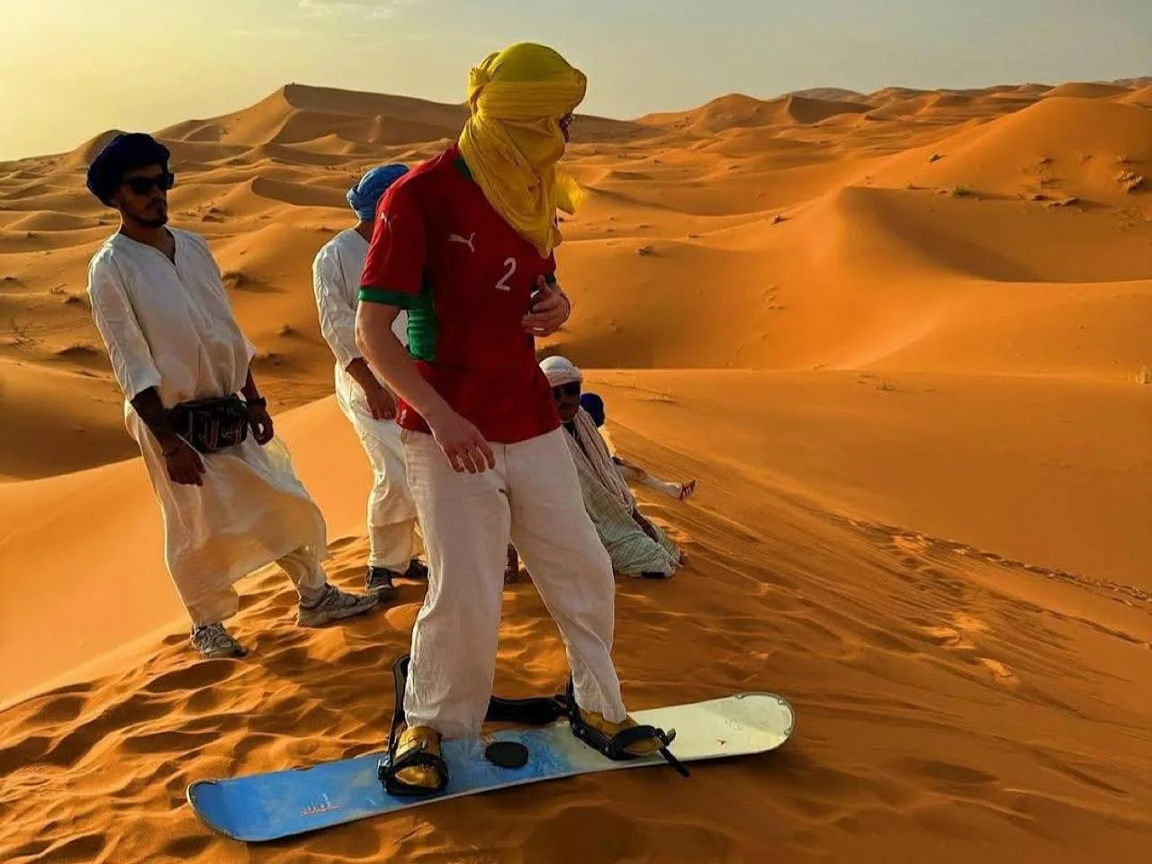 Guest sandboarding in the dunes near Gorgeous Luxury Camp in Merzouga during a desert activity.