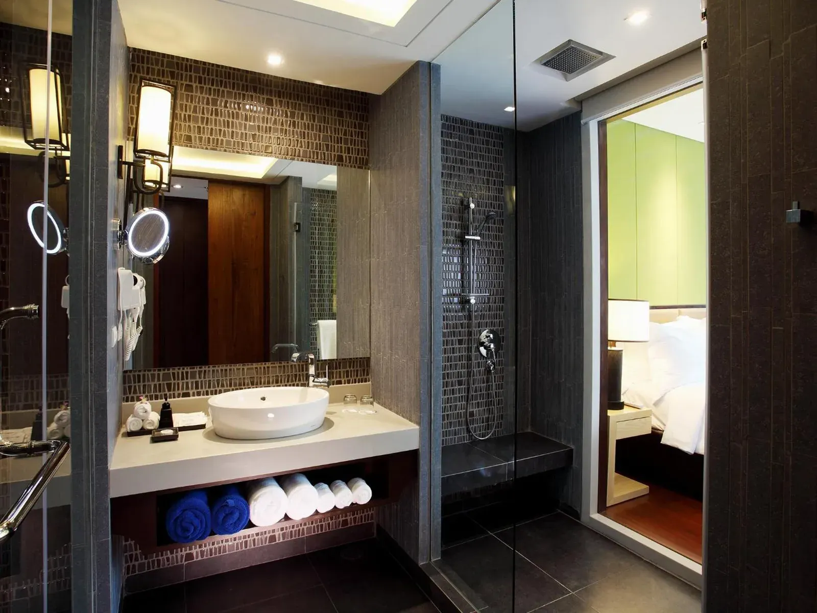 Baño con azulejos oscuros en Graceland Khaolak Beachfront Resort con ducha de lluvia, lavabo y espejo