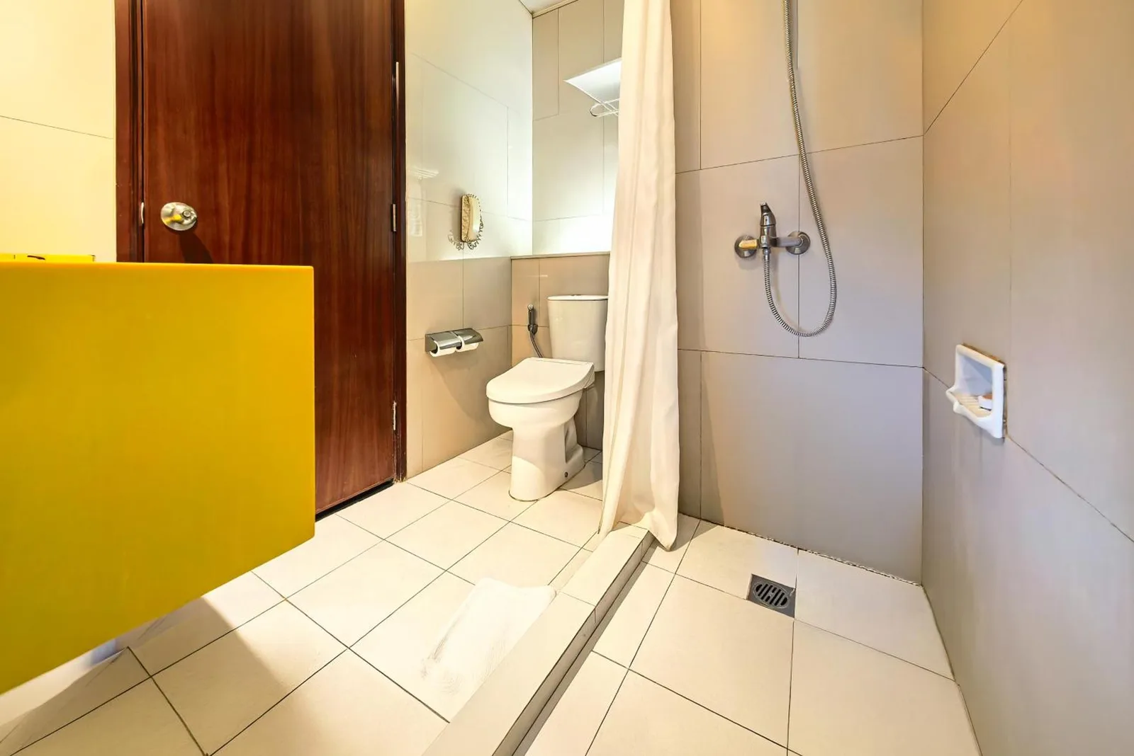 Douche et toilettes de salle de bains au Grand Candi Hotel Semarang avec zone humide carrelée