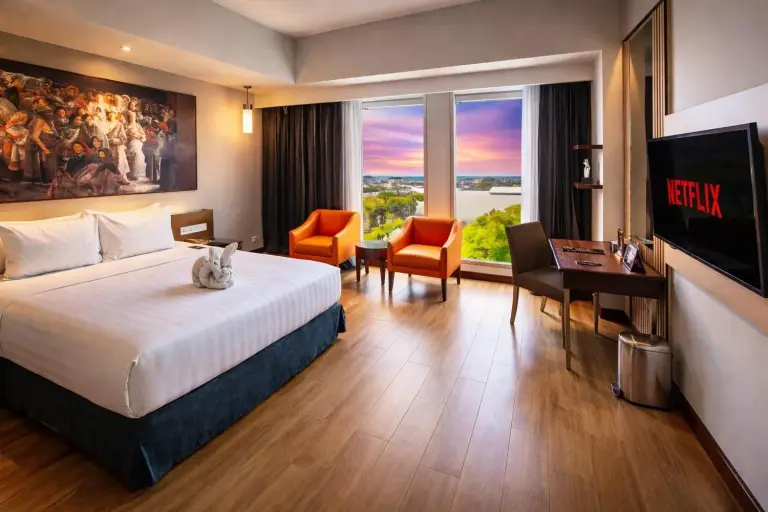 Chambre king au Grand Candi Hotel Semarang avec chaises orange, bureau et vue sur la ville