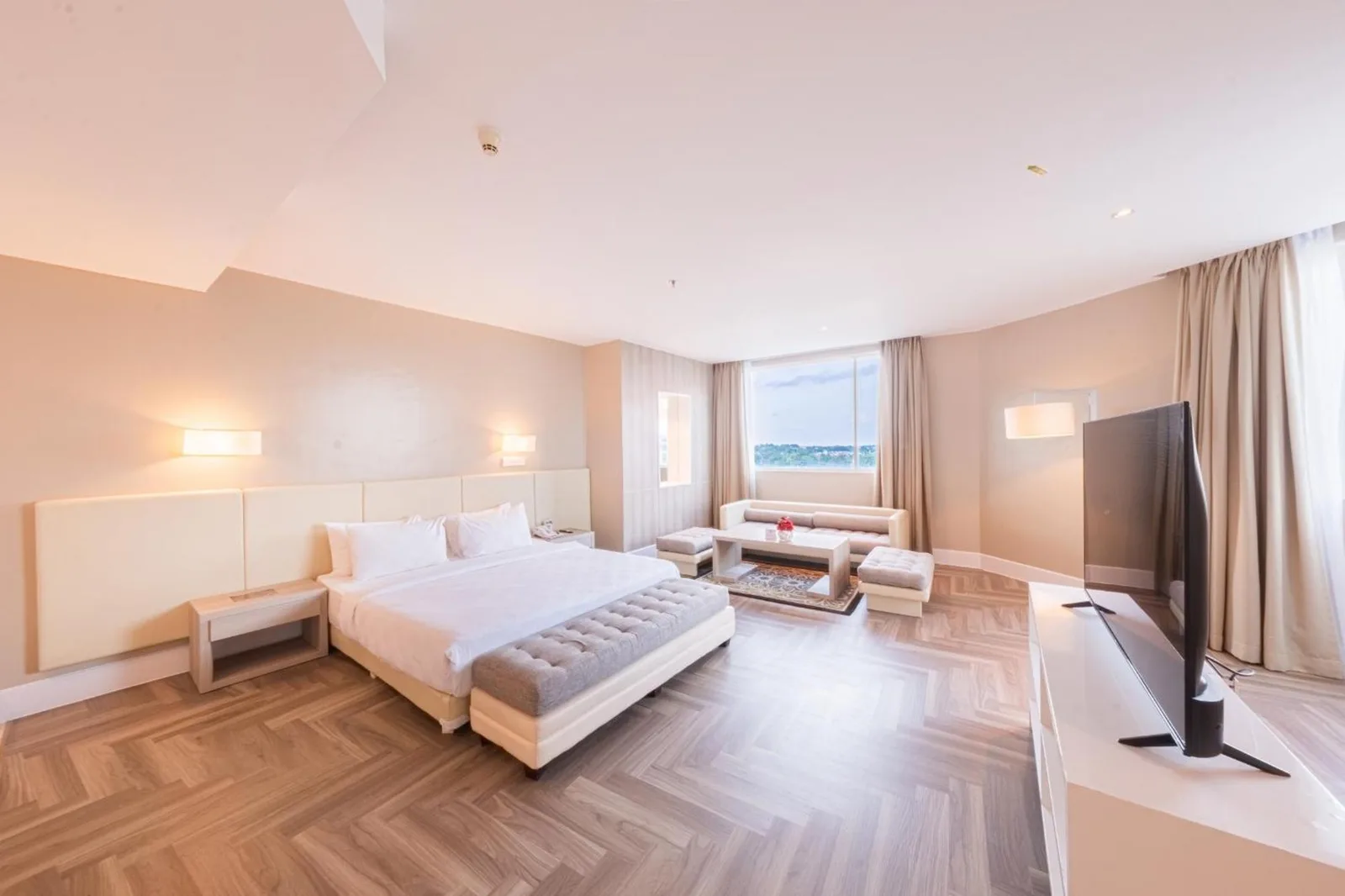 Corner suite at Grand Jatra Hotel Balikpapan with a bed, bench, sofa, and large window with city view