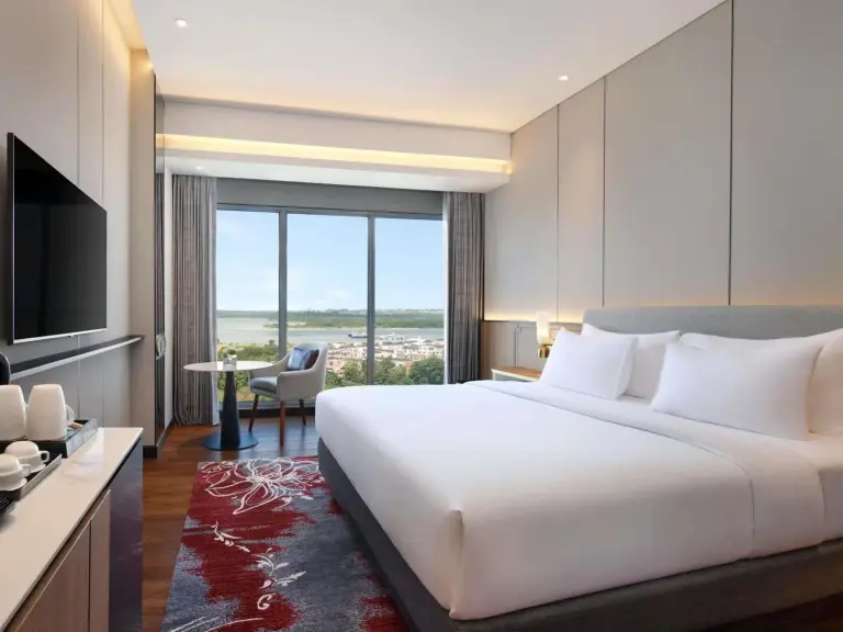 Habitación luminosa en Grand Mercure Batam Centre con cama king, TV y vistas desde ventanales de suelo a techo.