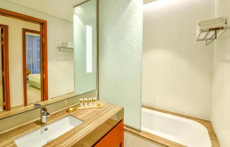 Badezimmer im Grand Mercure Dubai City mit Waschtisch, Spiegel, Badewanne und modernen Oberflächen