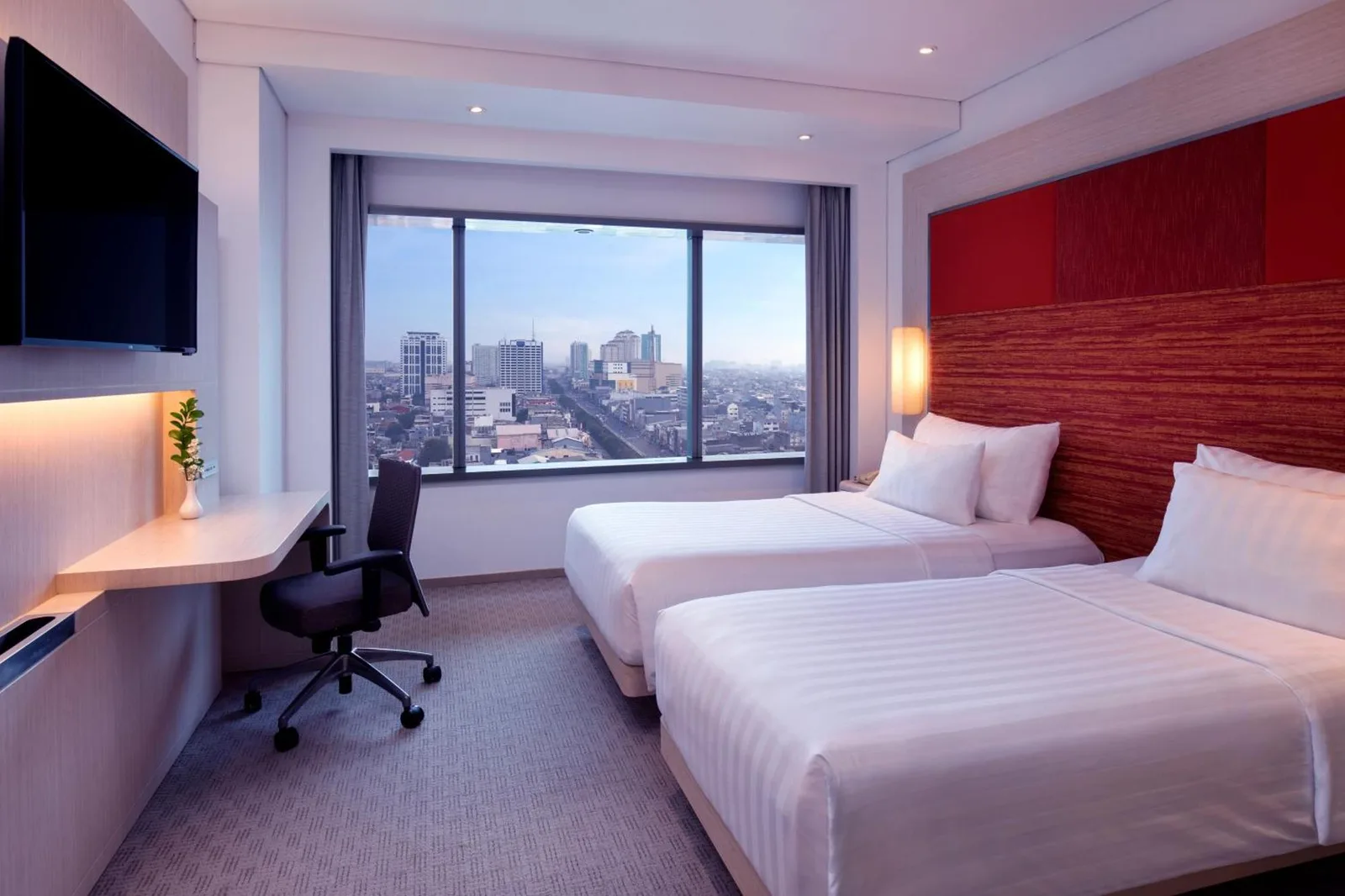 Gästezimmer mit Kingsize-Bett im Grand Mercure Jakarta Harmoni mit Fenster zur Skyline der Stadt und Sitzbereich
