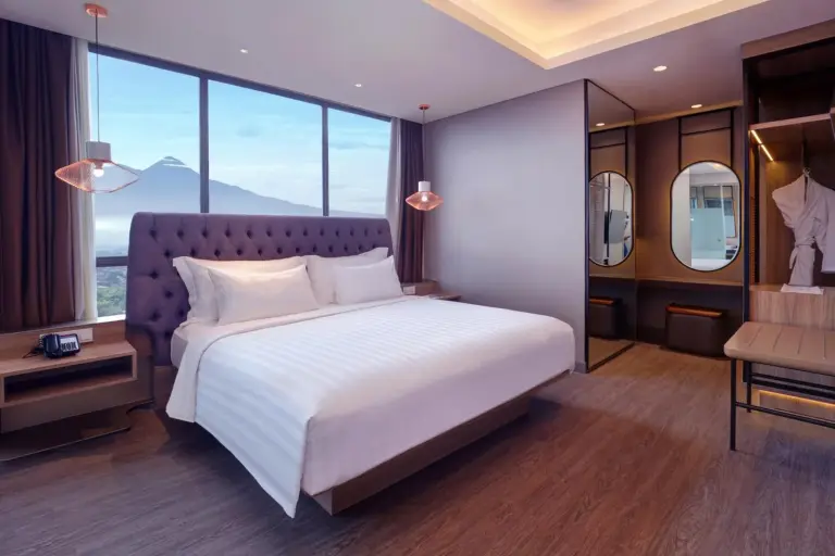 Elegante dormitorio en Grand Mercure Malang Mirama en Malang con cabecero capitoné y vistas a la montaña