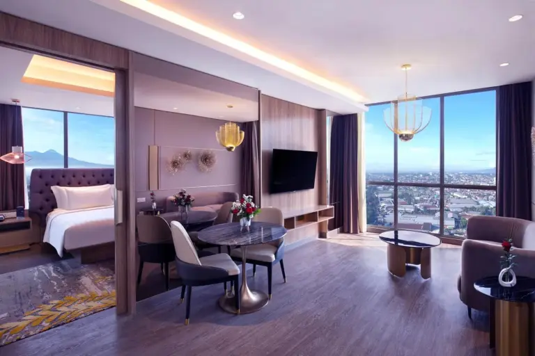 Amplia sala de estar de una suite en Grand Mercure Malang Mirama en Malang con mesa de comedor y ventanal panorámico