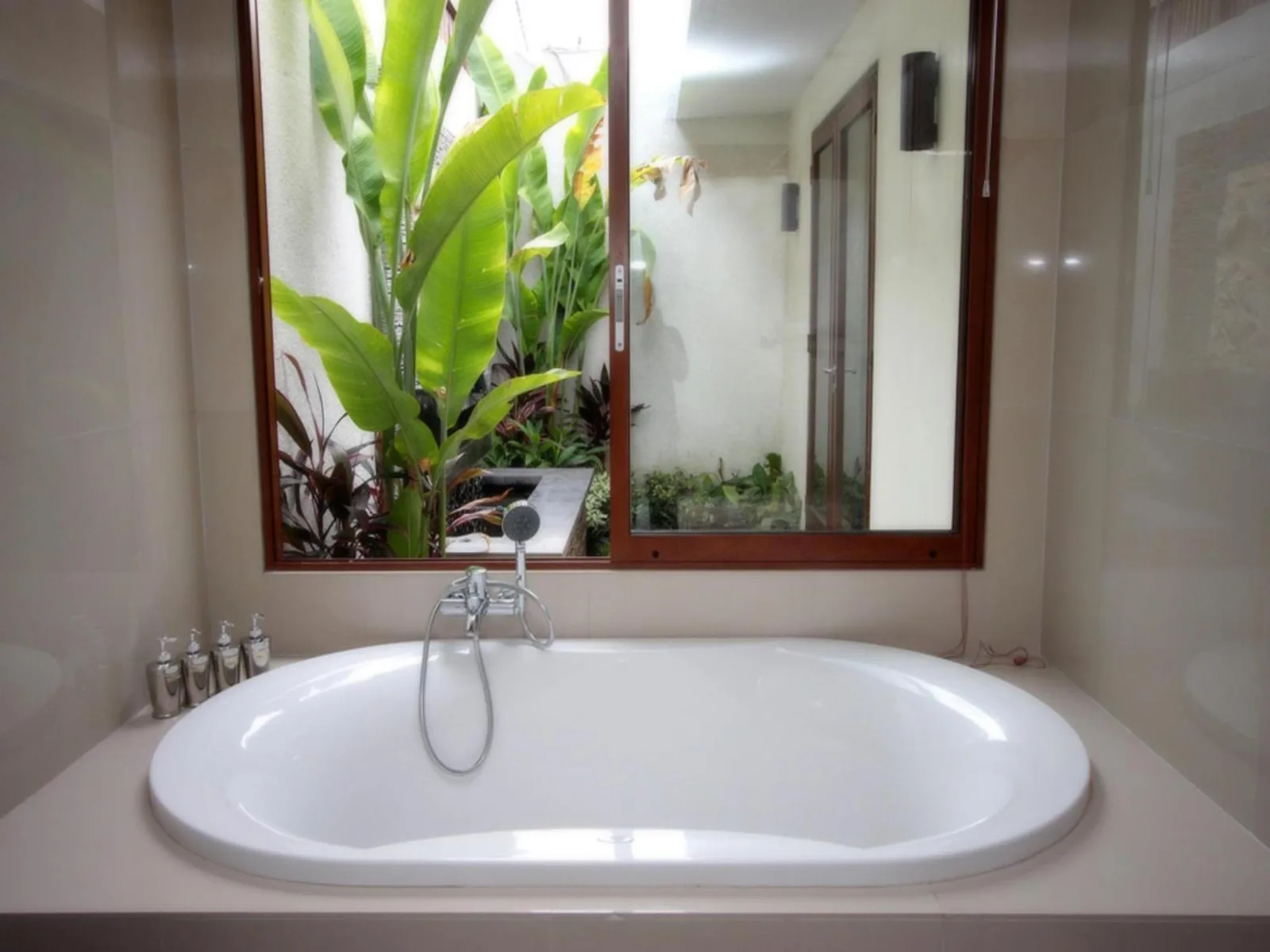 Bathtub in a bathroom at Grania Bali Villas in Seminyak with a view of tropical greenery.