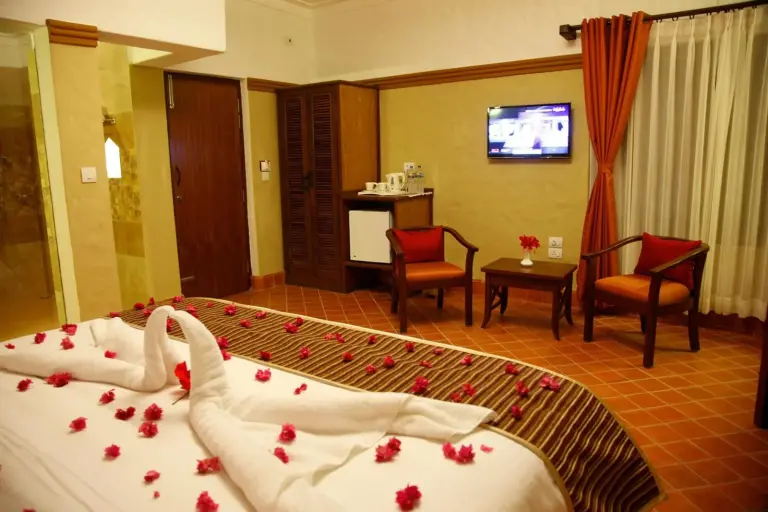 Chambre d’hôtes à l’hôtel Green Park Chitwan à Sauraha avec deux fauteuils, télévision et portes donnant sur la terrasse.