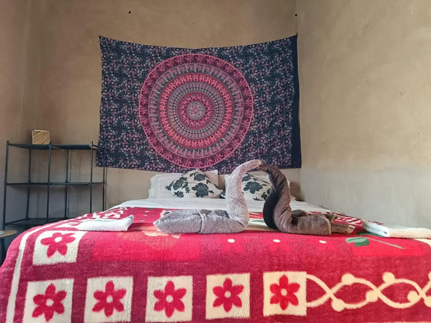 Nahaufnahme dekorativer Handtuchschwäne auf einem Bett im Guest House Nomad Life in Merzouga mit Lampe und Regal im Hintergrund.