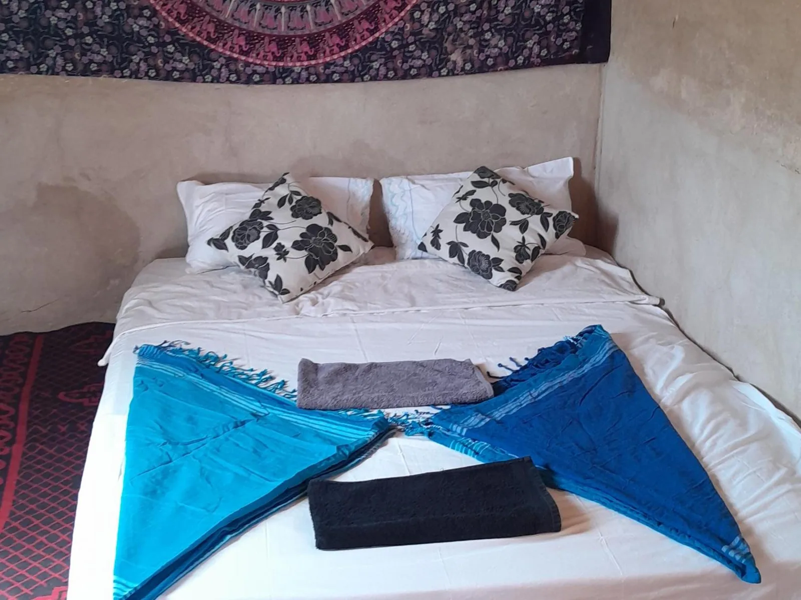 Doppelbett im Guest House Nomad Life in Merzouga mit weißer Bettwäsche, floralen Kissen und dekorativen Handtüchern.
