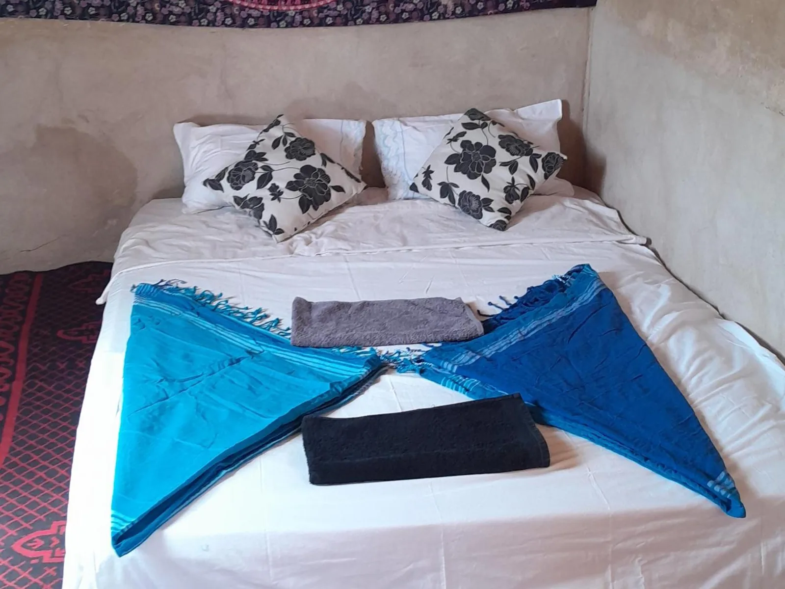 Zwei Betten in einem Zimmer im Guest House Nomad Life in Merzouga mit dekorativen Handtüchern und gemustertem Wandbehang.