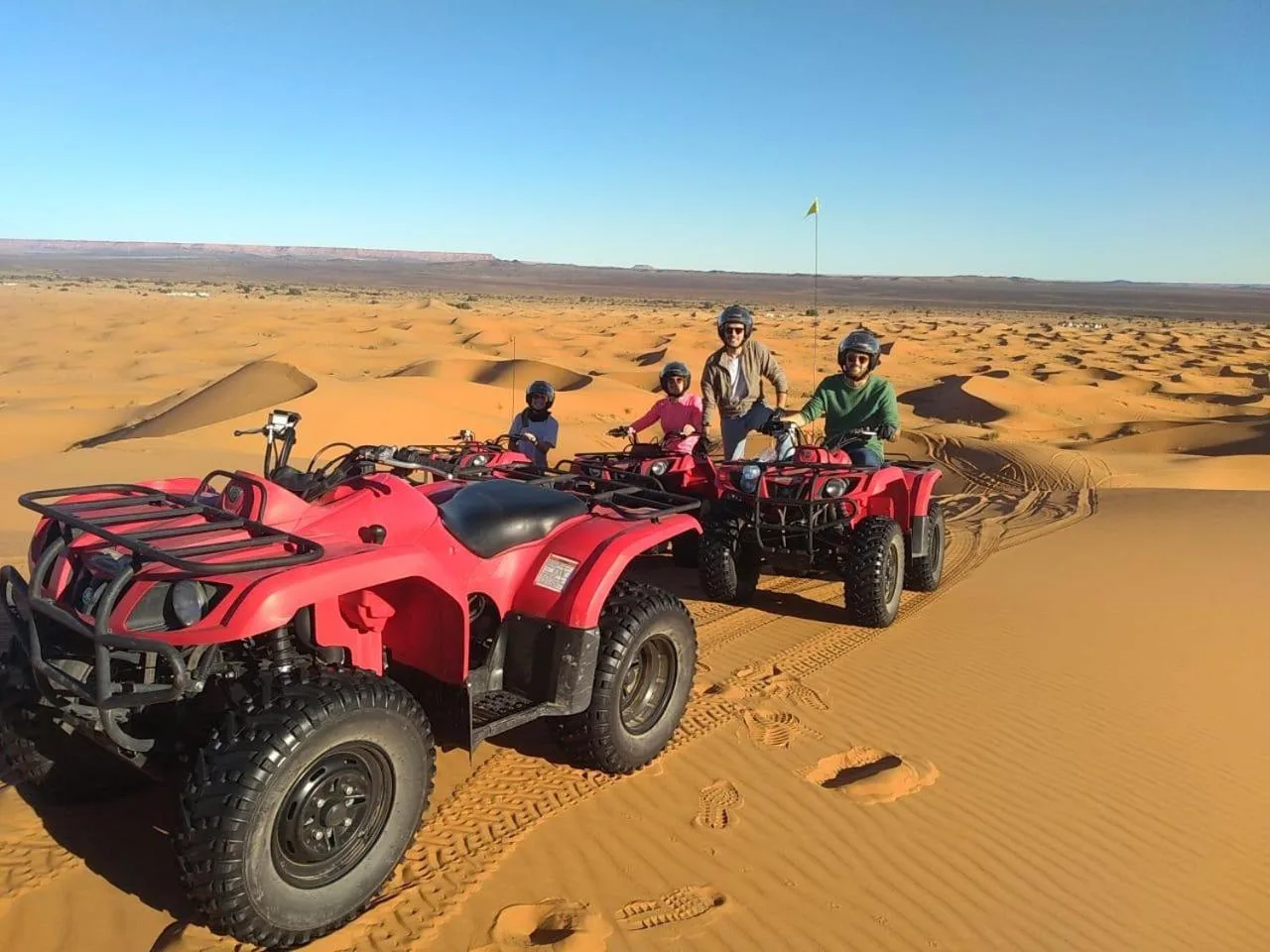 Guests riding red ATVs in the desert near Guests House in Merzouga with sand dunes in the background.