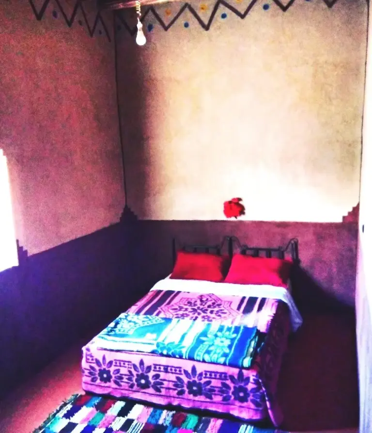 Single room at Guests House in Merzouga with a bed, colorful bedding, and traditional wall decor.